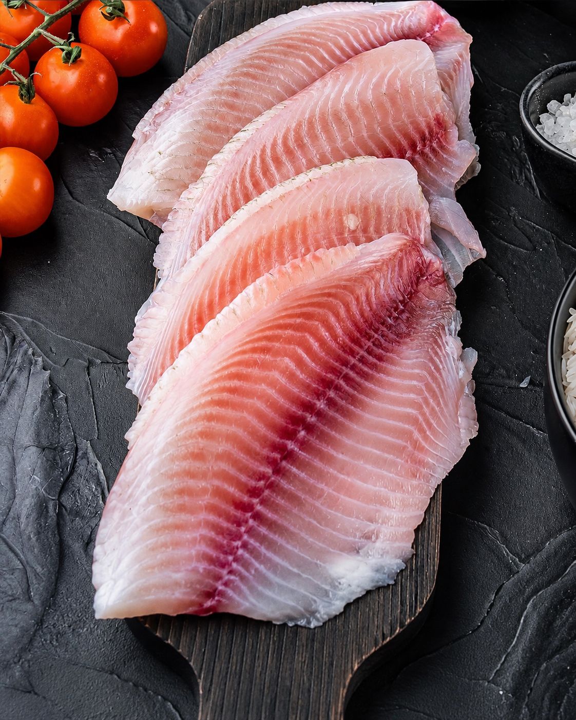 Filés de pescado fresco com tomates e ervas sobre tábua escura